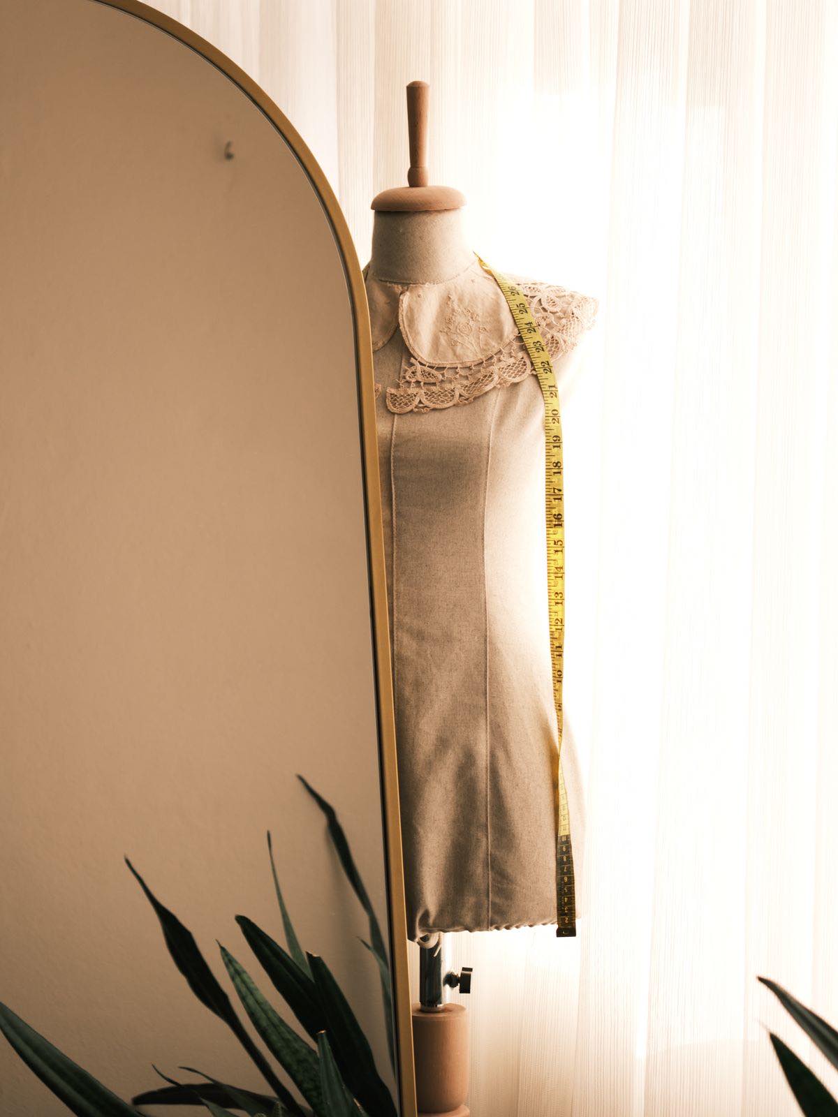 A linen dressmaker's stand with a lace collar and a tape measure, in warm window light