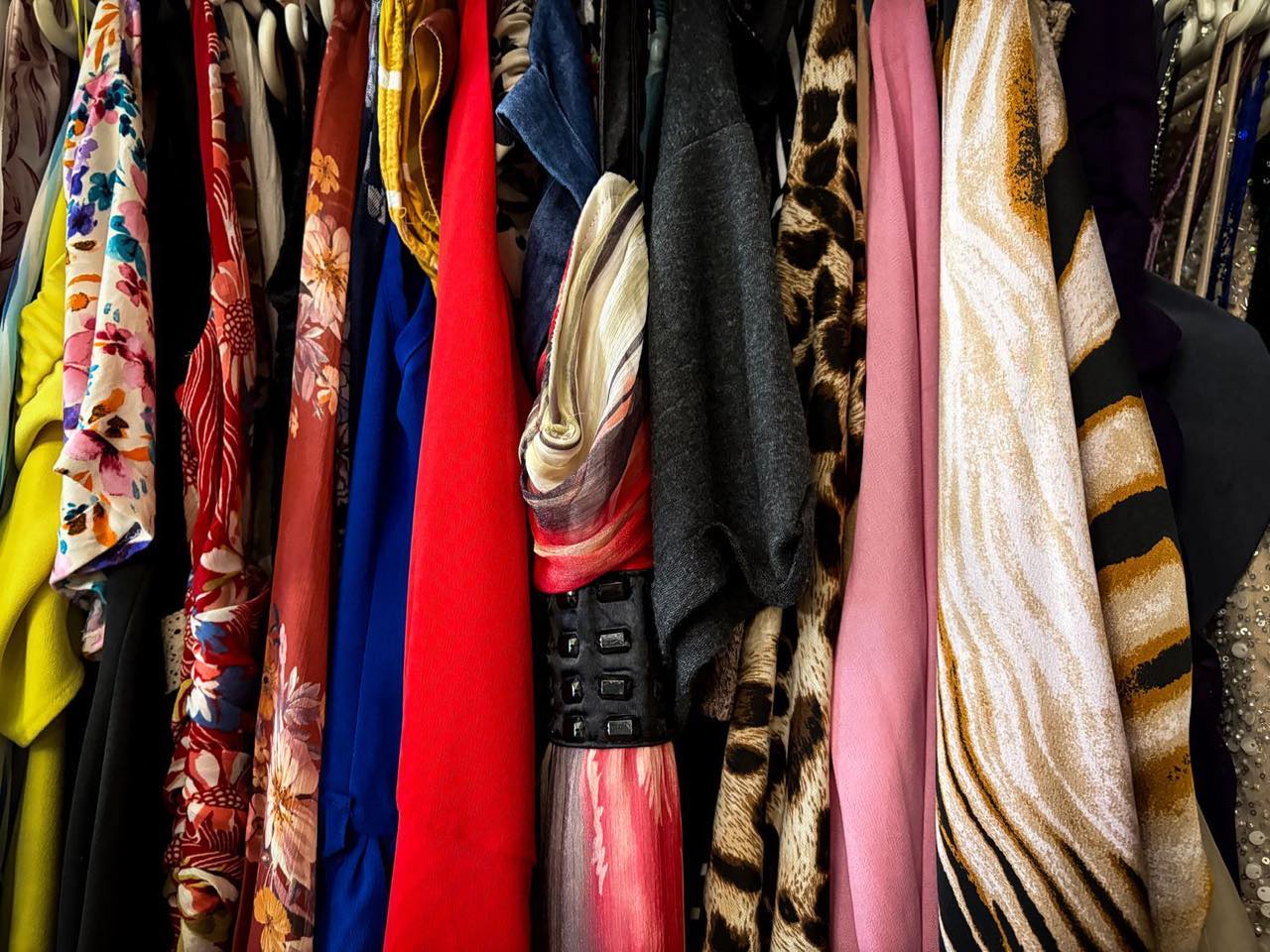 A densely packed rack of patterned vintage dresses, scarves and knitwear