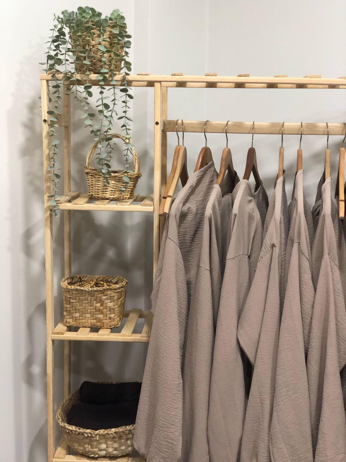 Linen pieces on a wooden clothes rack beside wooden shelving with woven baskets