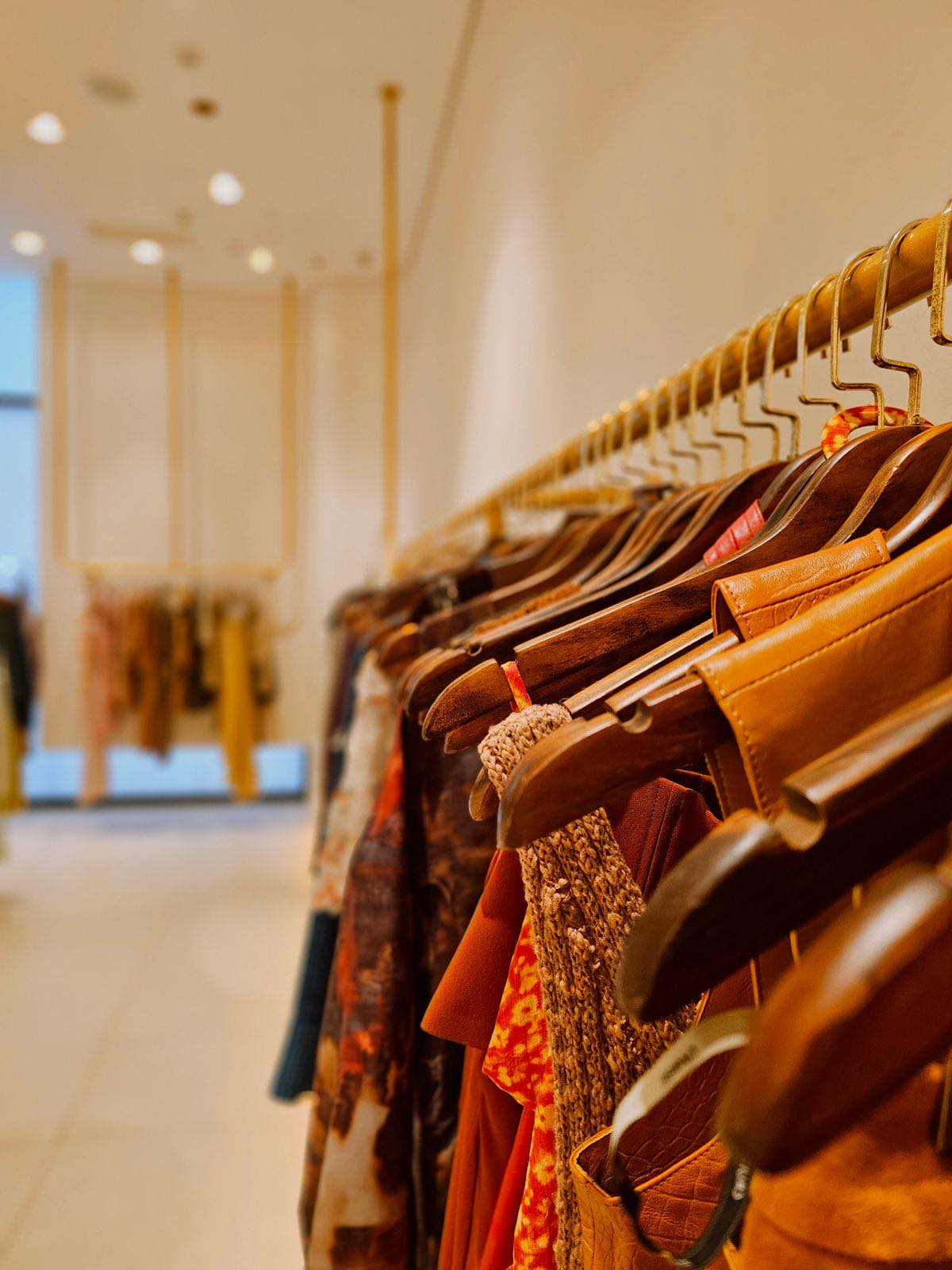 Vintage coats and knitwear on wooden hangers in a warmly lit shop